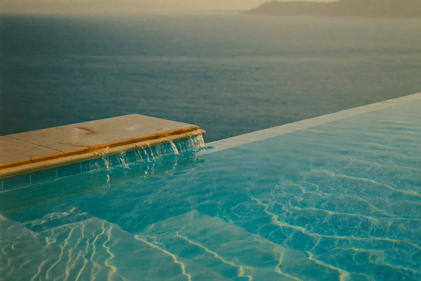 A villa pool at dusk with the underwater lights on.