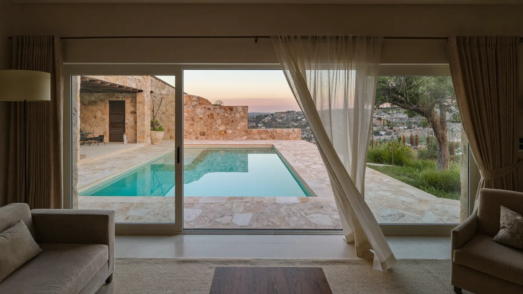 A quiet villa living room at dawn, the doors open onto a still pool.